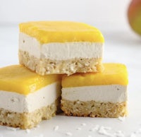 a stack of mango cheesecake bars on a white surface